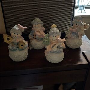 4 snowman figurines. All are holding birds except one holding bird houses.